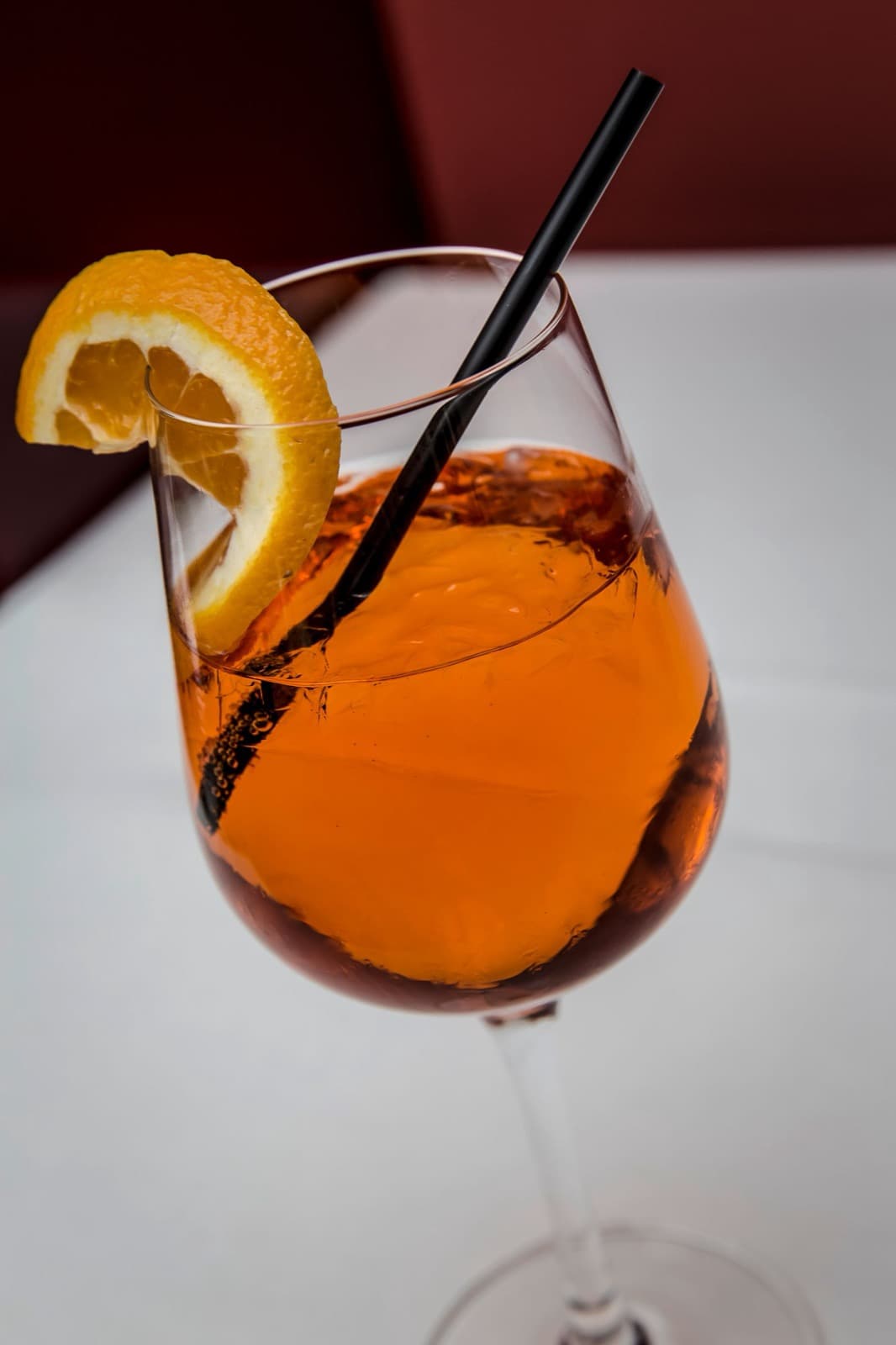 An orange Aperol spritz in a wine glass with an orange slice and a black straw
