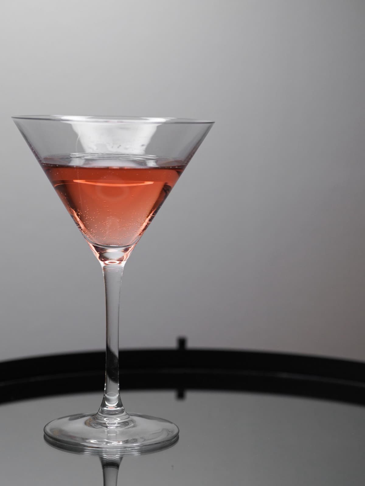 A pale pink cosmopolitan in a classic martini glass against a soft grey studio background