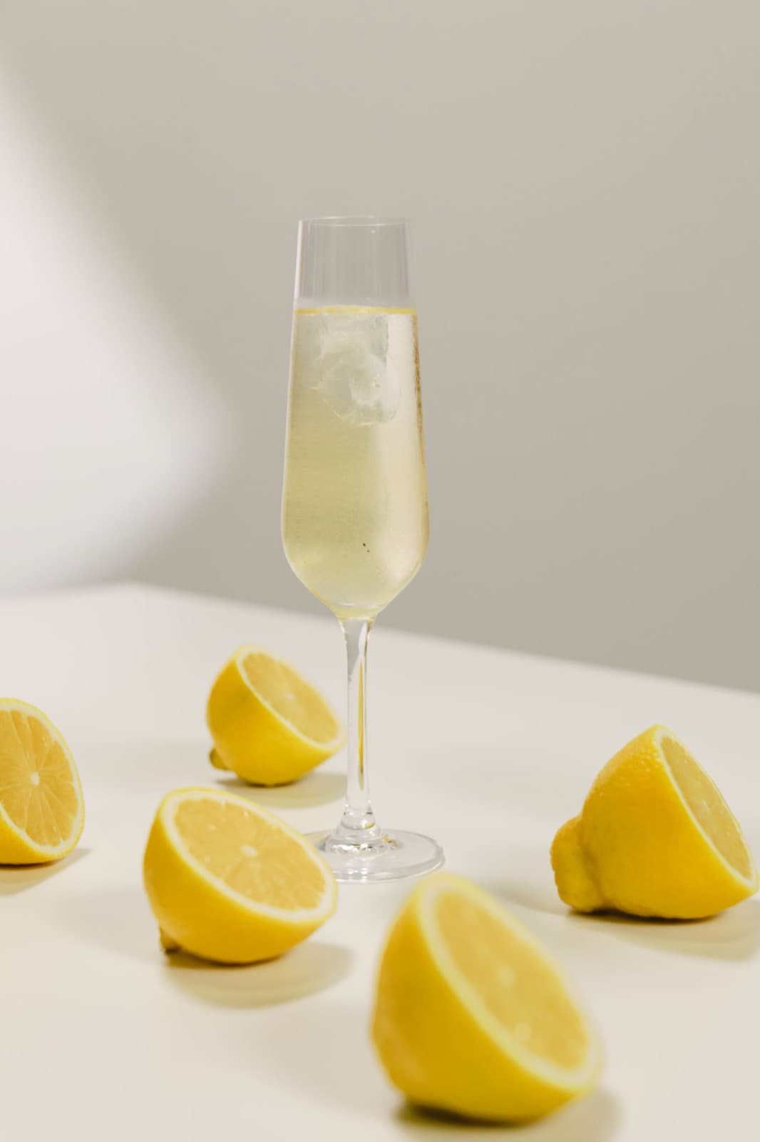 A French 75 in a champagne flute surrounded by halved lemons on a white table