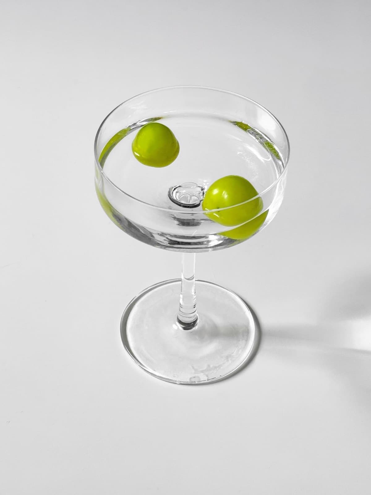 A clear martini in a coupe with two green olives, on a white background