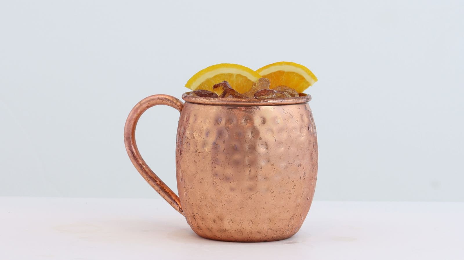 A Moscow mule in a hammered copper mug topped with citrus slices, on a white background