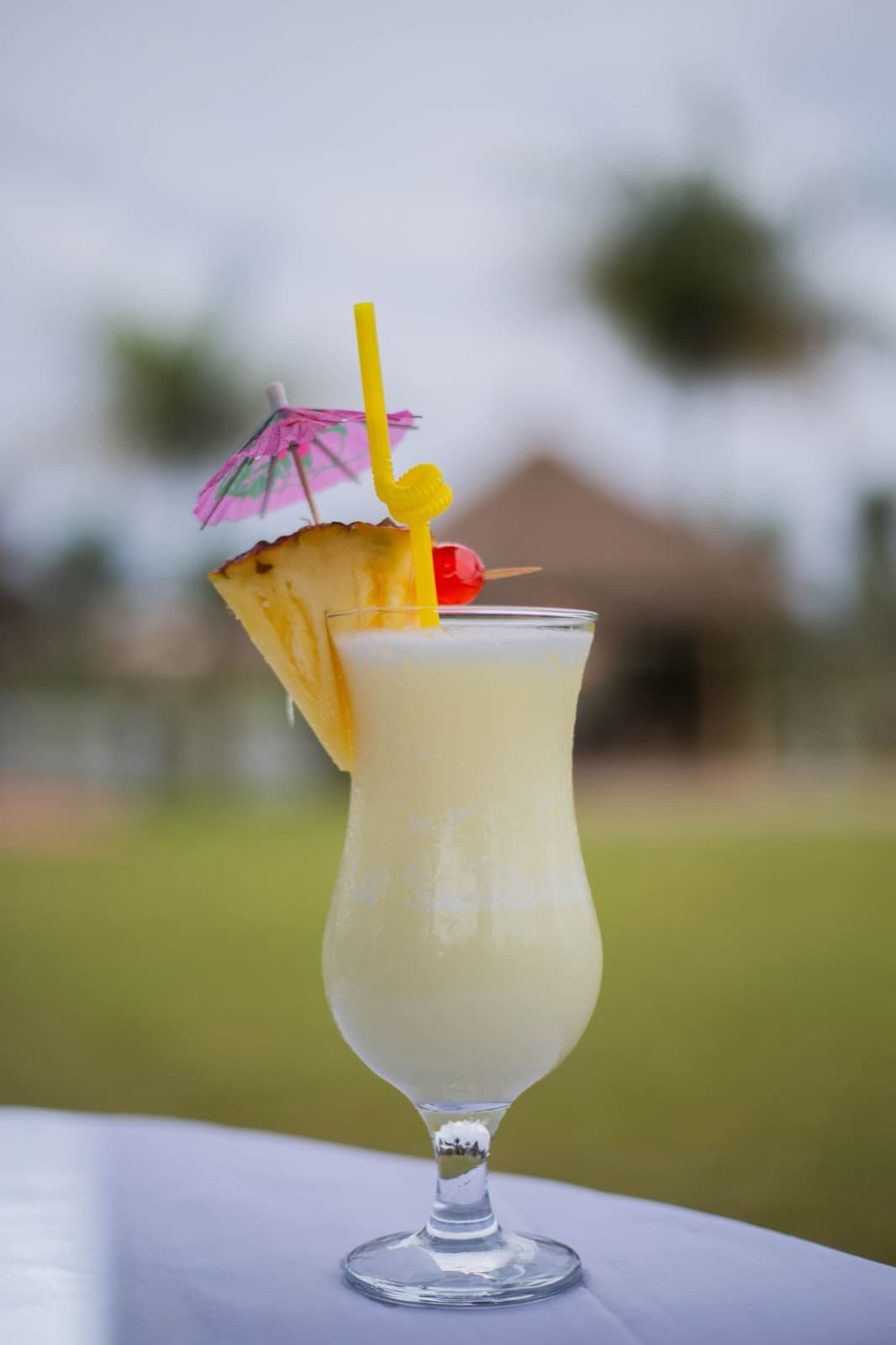 A frozen piña colada in a hurricane glass with a pineapple wedge, cherry and paper umbrella, outdoors in soft daylight