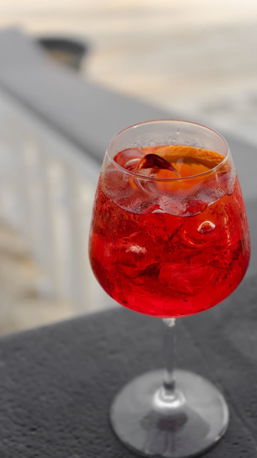 A red spritz over ice in a large wine glass with an orange slice, on a sunny terrace ledge