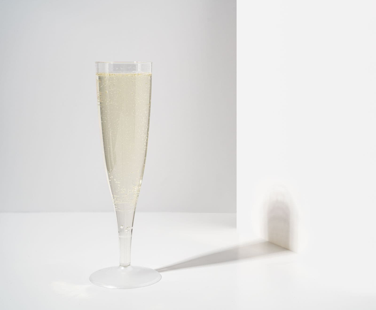 A flute of sparkling wine with rising bubbles, casting a soft shadow on a white background