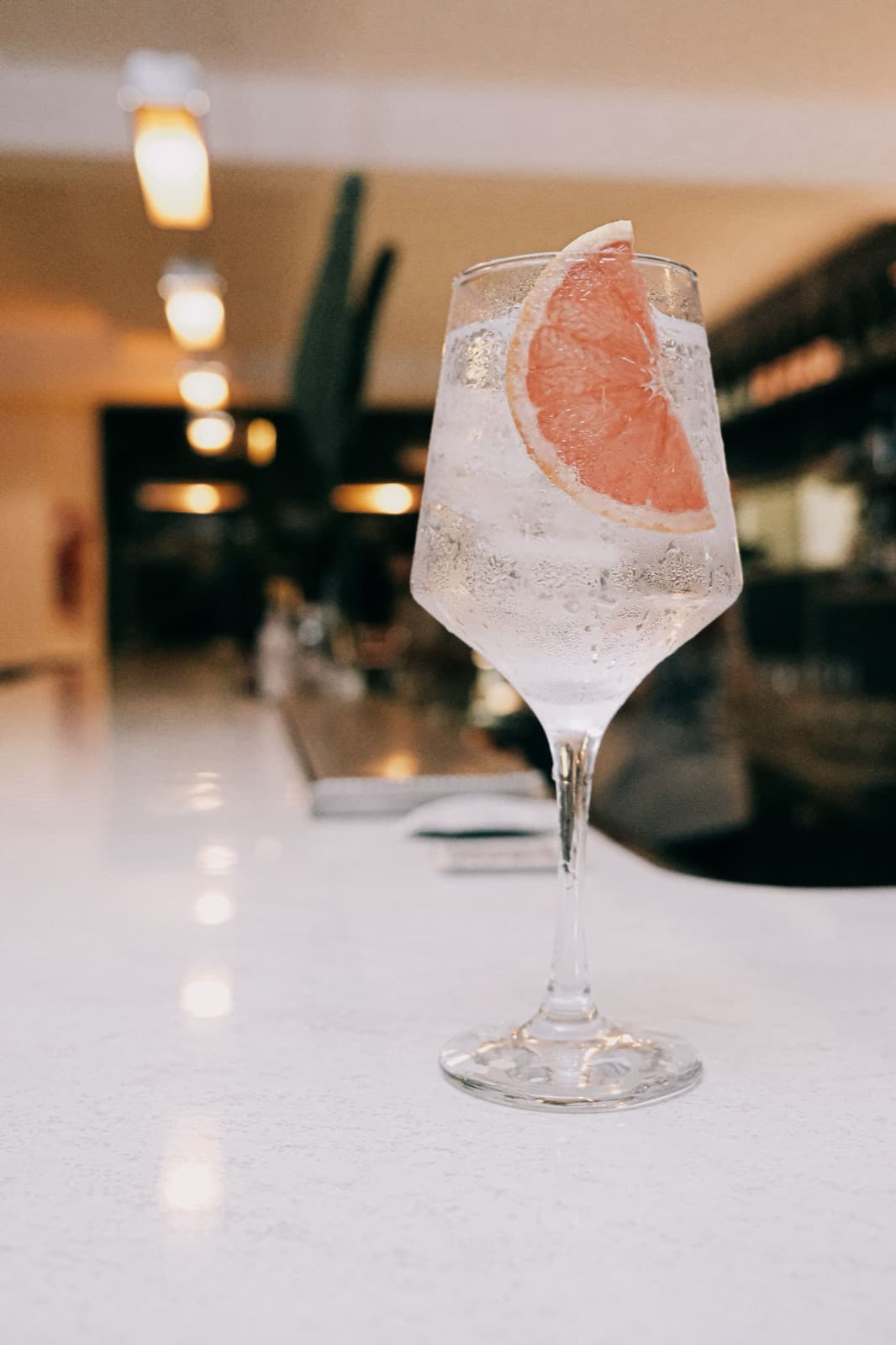 A gin and tonic over ice in a stemmed copa glass with a pink grapefruit slice, on a pale counter